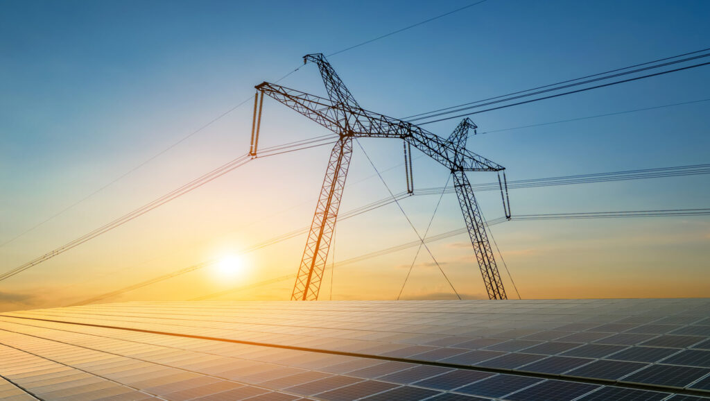 High voltage pylons with electric power lines transfering electricity from solar photovoltaic sells at sunrise. Production of sustainable energy concept.